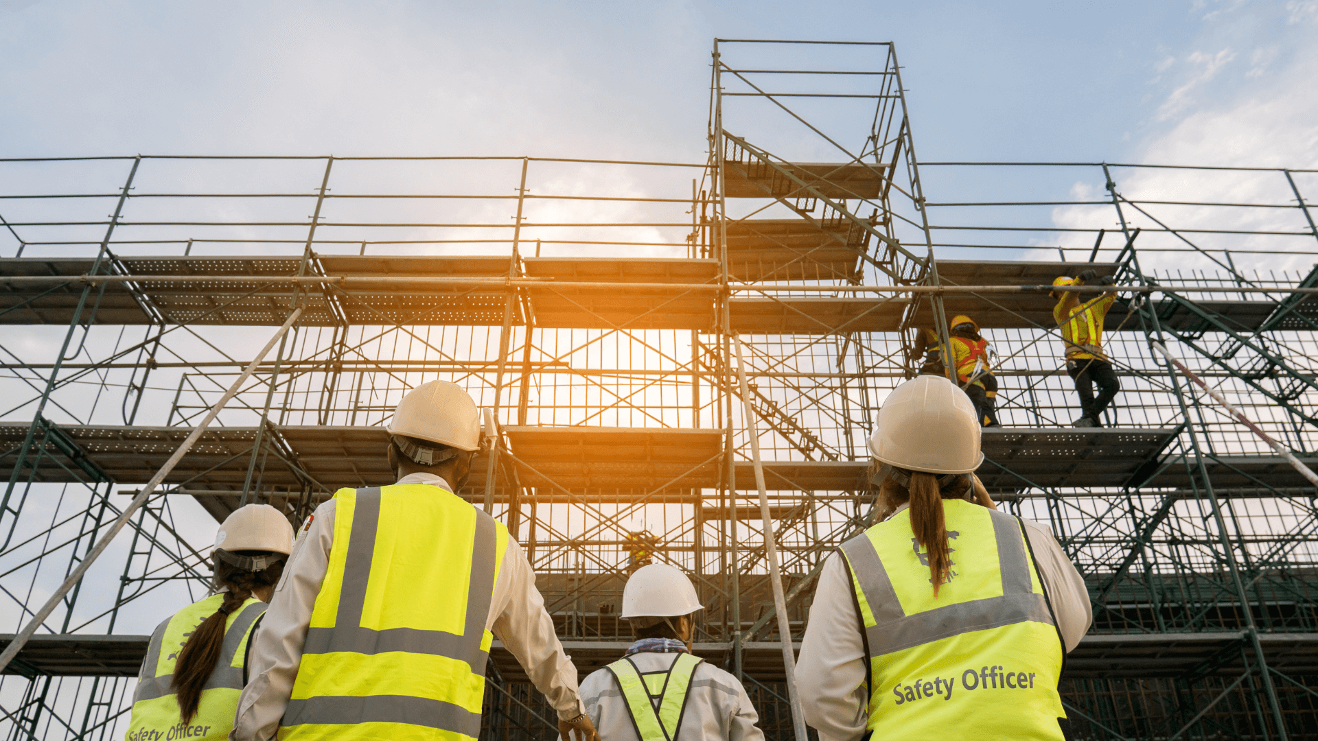 Safety officers in high visibility clothing looking at workers on scaffolding