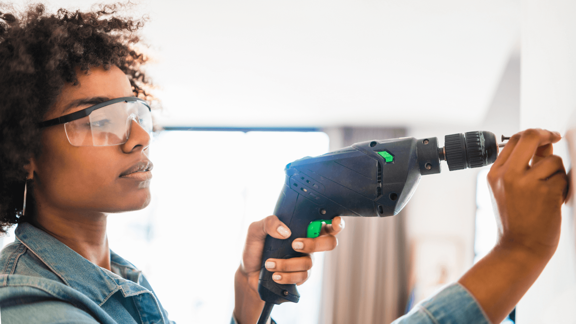 Woman in safety glasses drilling into wall