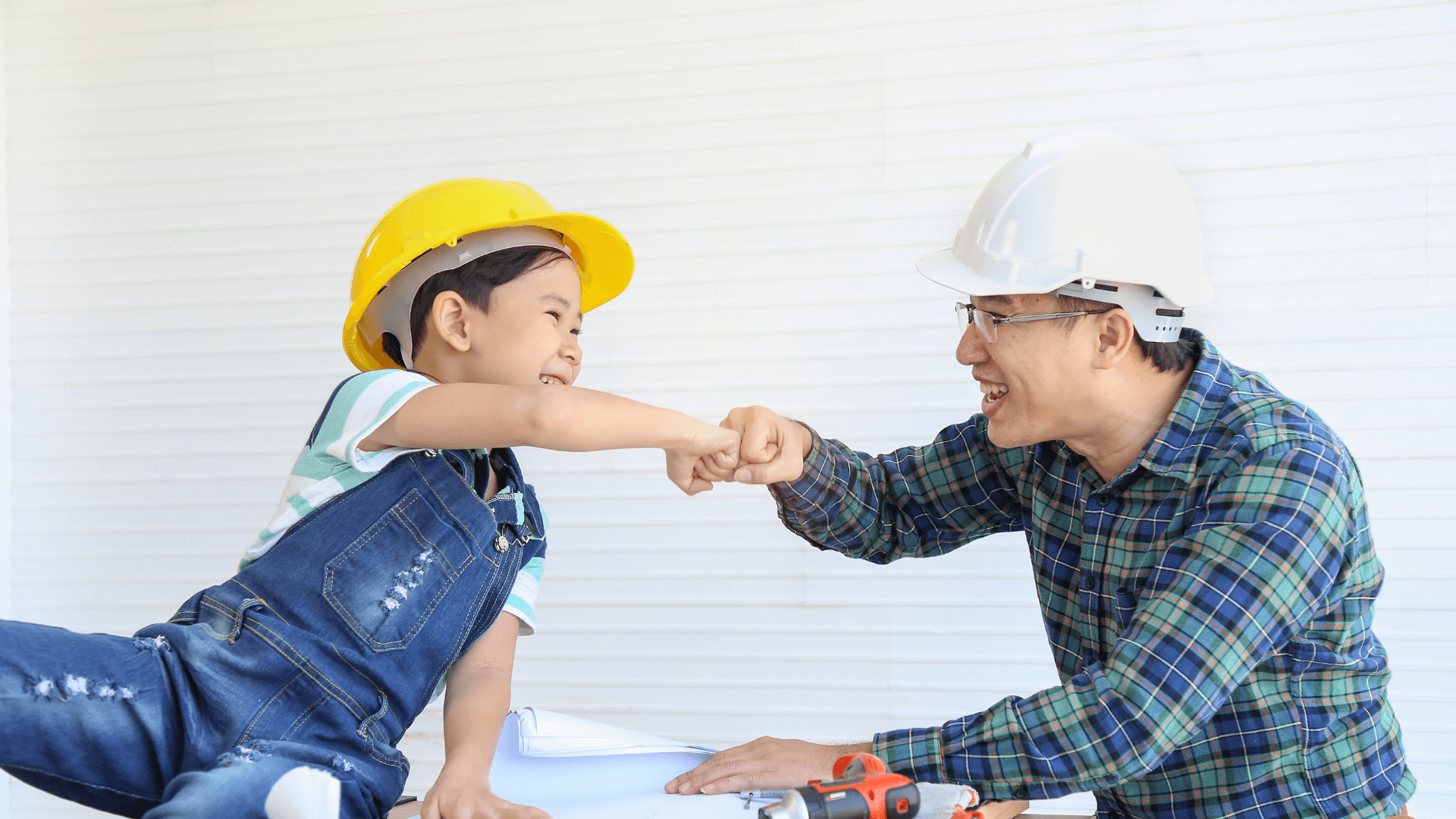 Father and son in hard hats looking at plans fist bumping