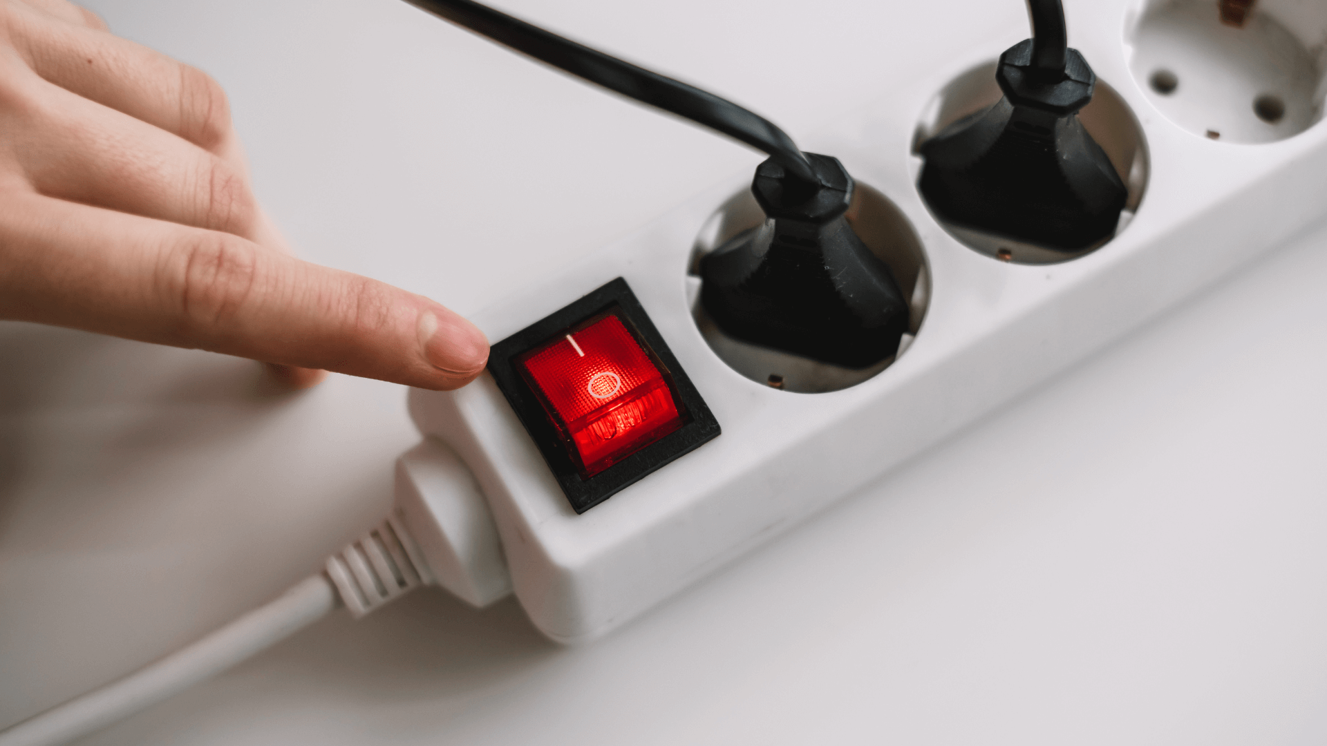 Electricity extension cord with two plugs in, finger on switch