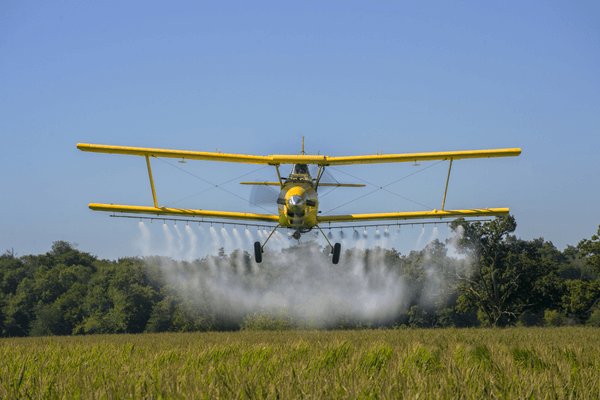 Yellow crop duster flying over agricultural field