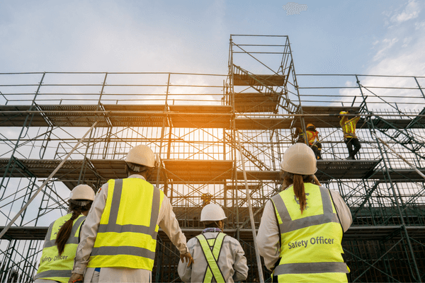 Safety officers in high visibility clothing looking at workers on scaffolding