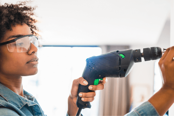 Woman in safety glasses drilling into wall