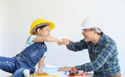Father and son in hard hats looking at planning material fist bumping