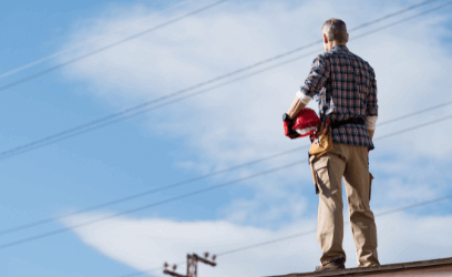 Man standing on roof holding hard hat looking at overhead electricity wires 